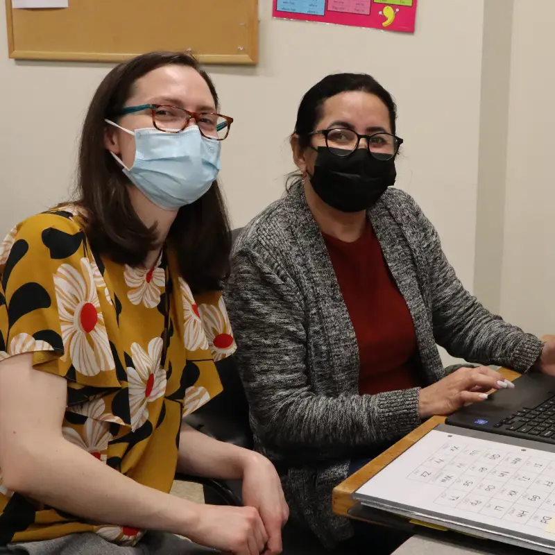 Two women wearing masks at a desk